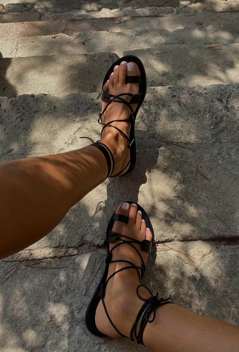 Black lace-up sandals with sheer white nail colour on toes