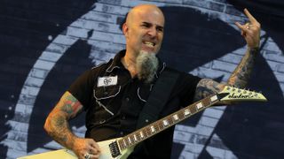 A photograph of Scott Ian on stage, giving the horns with a guitar, in 2015