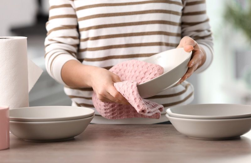 A person drying dishes with a kitchen towel.