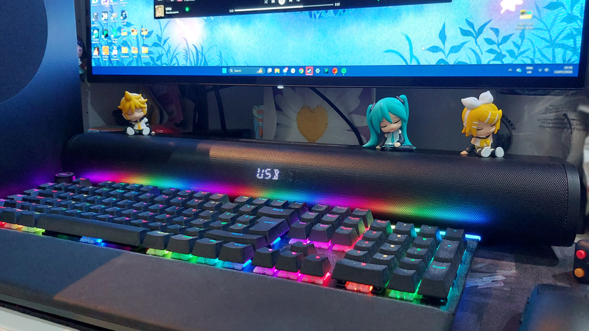 The Creative Stage Pro sits on a desk before a monitor and behind an RGB keyboard. Miniature Vocaloid figurines sit along the top of the soundbar. The soundbar&#039;s LED display shows the device is in USB mode.