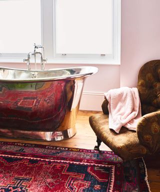 A reflective tin bath with magenta pink patterned rug and brown peacock print armchair
