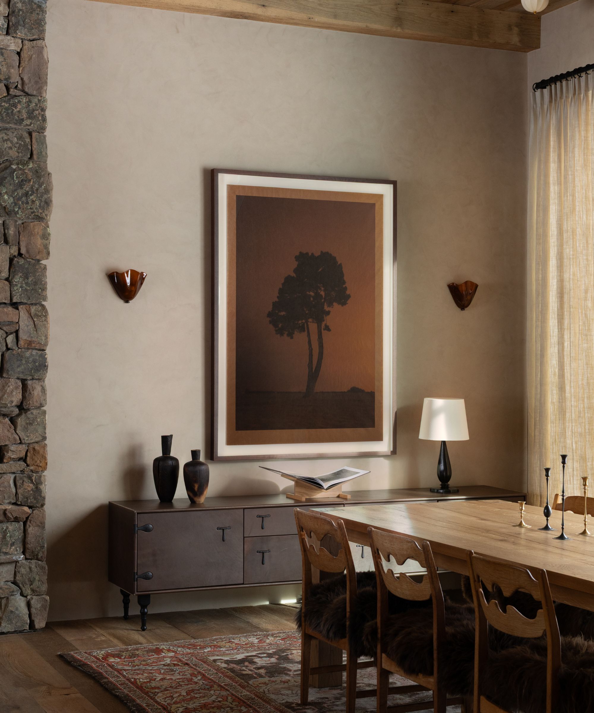 a stone plastered dining room with a wooden clad ceiling, stone wall, vintage rug and chairs, with a large tree wall art