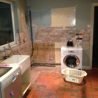 kitchen area with break wall and red tiles flooring with washing machine and plastic basket