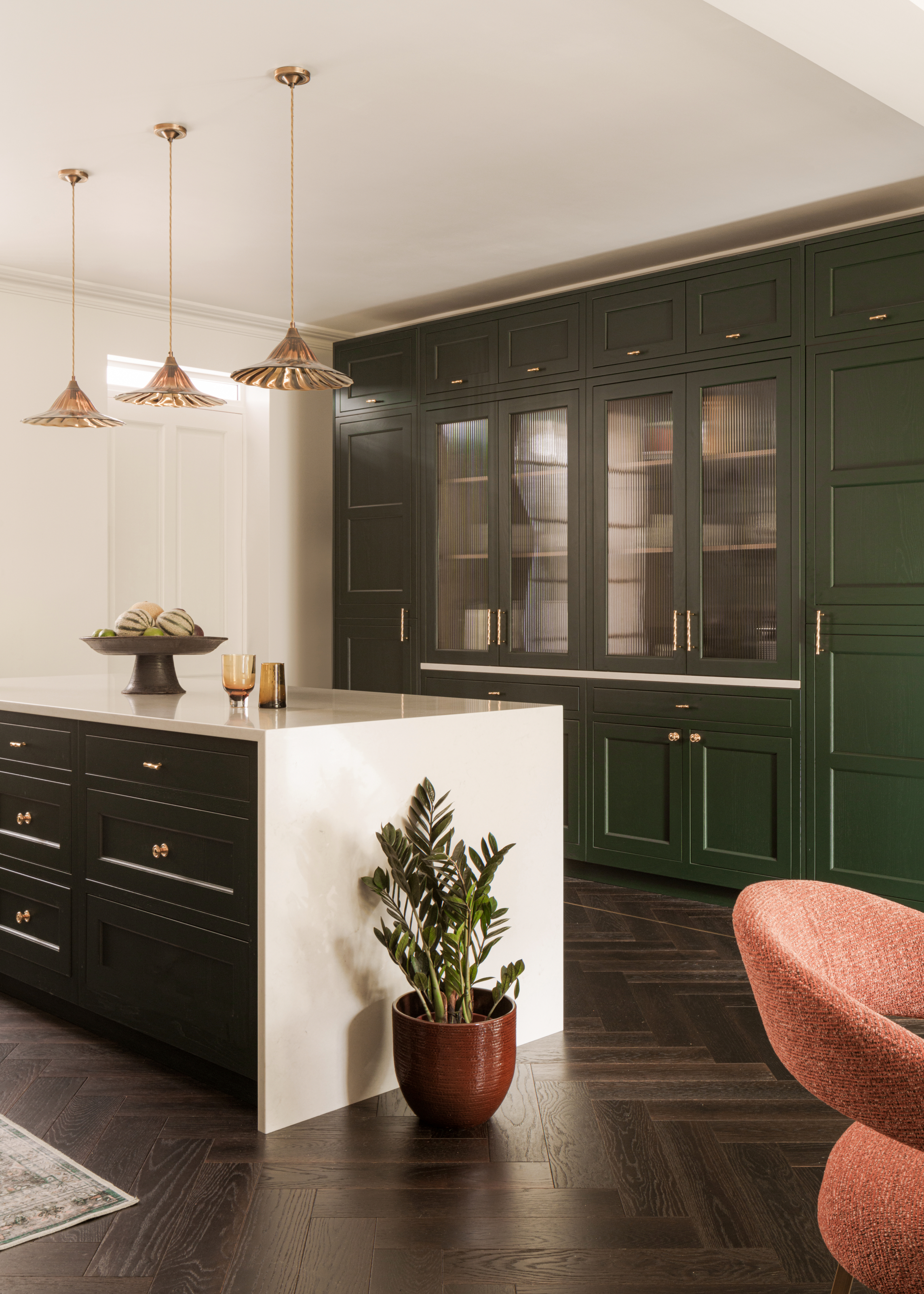 Green Shaker-style kitchen with dark wood herringbone floor and white stone island countertop