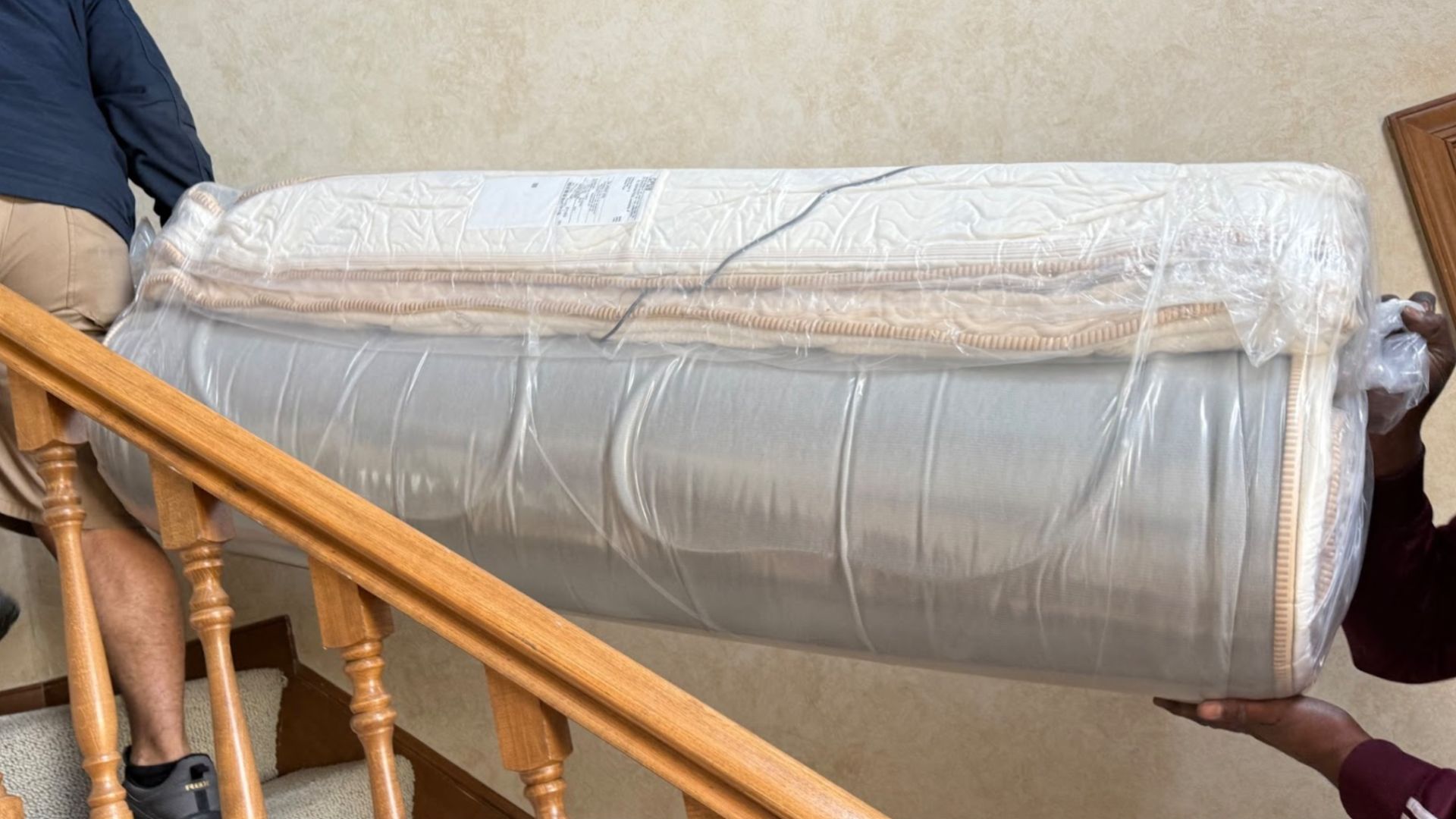 Two men carrying the rolled and packaged Saatva Solaire mattress up stairs