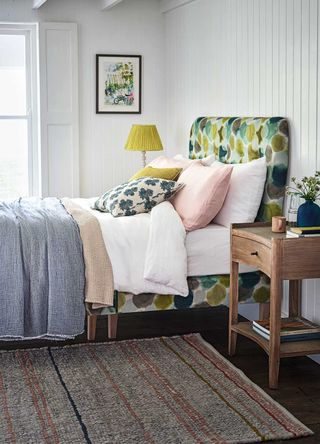 pale grey bedroom with green patterned upholstered bed with yellow accent cushions and fresh white bedding