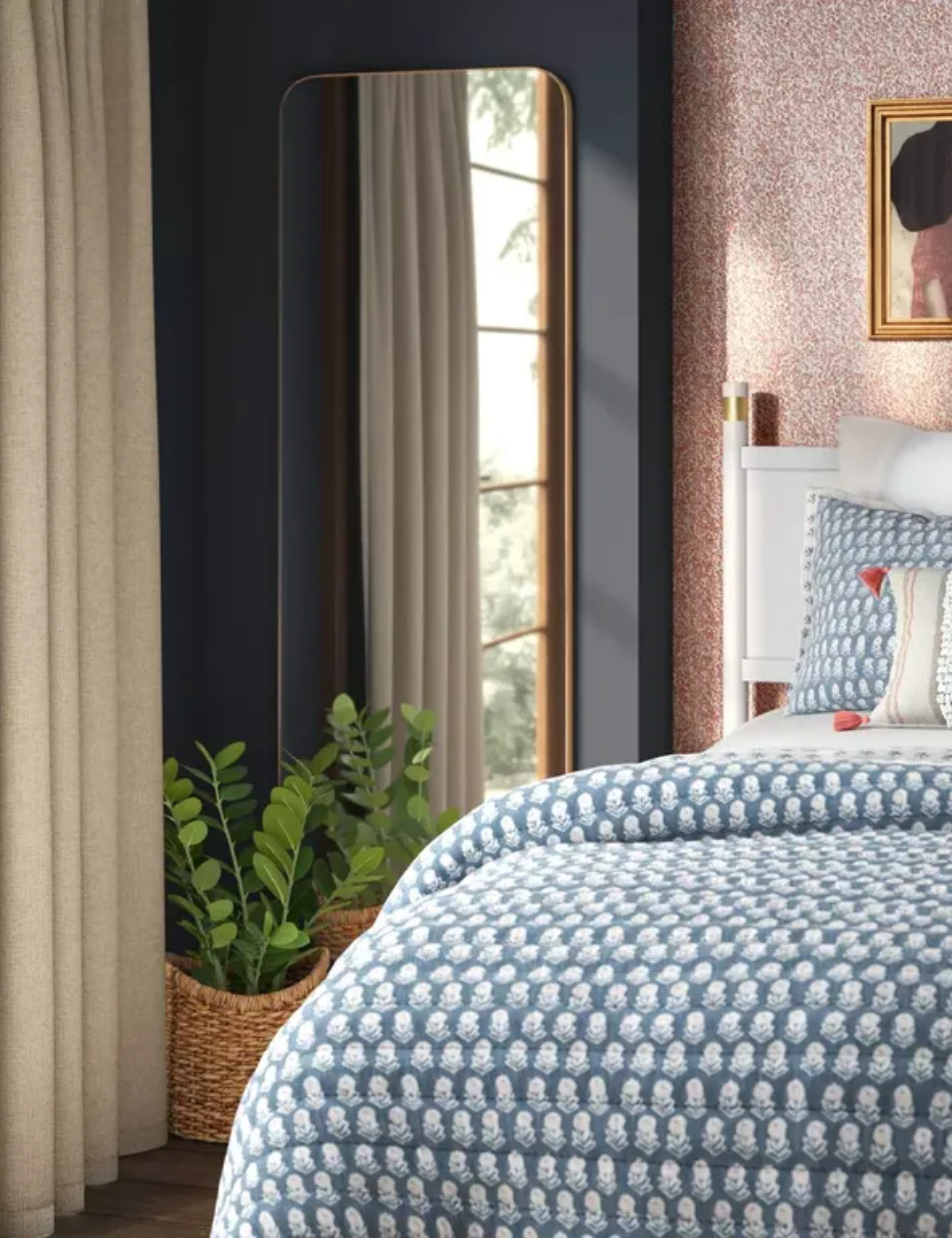 Floor mirror in a pattern filled bedroom with wall art and tassled accent pillows