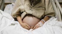 photo of a pregnant woman's belly as she's sitting on a hospital bed with an IV in her hand