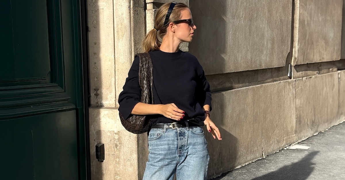 Danish fashion creative Clara Dyrhauge poses on a Paris sidewalk wearing a black headband, sunglasses, a black crewneck sweater, woven brown Bottega Veneta shoulder bag, a black belt, and jeans