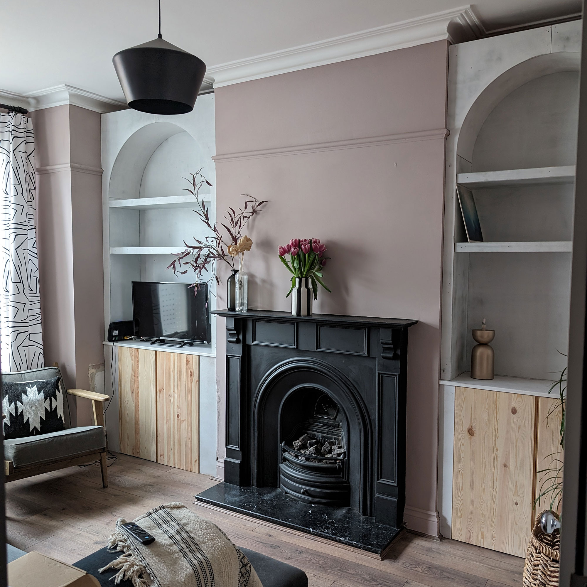 Pale pink living room with arched built-in bookcases mid being constructed on either side of black fireplace