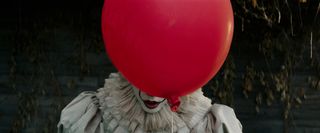 A red balloon obscures the face of Pennywise the Clown (Bill Skarsgård) in It.