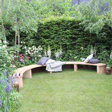 A small curved bench at the RHS Chelsea Flower Show, bookended with two trees