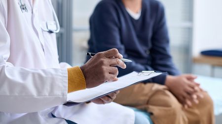 Side view closeup of a doctor holding a clipboard while consulting child in clinic copy space.