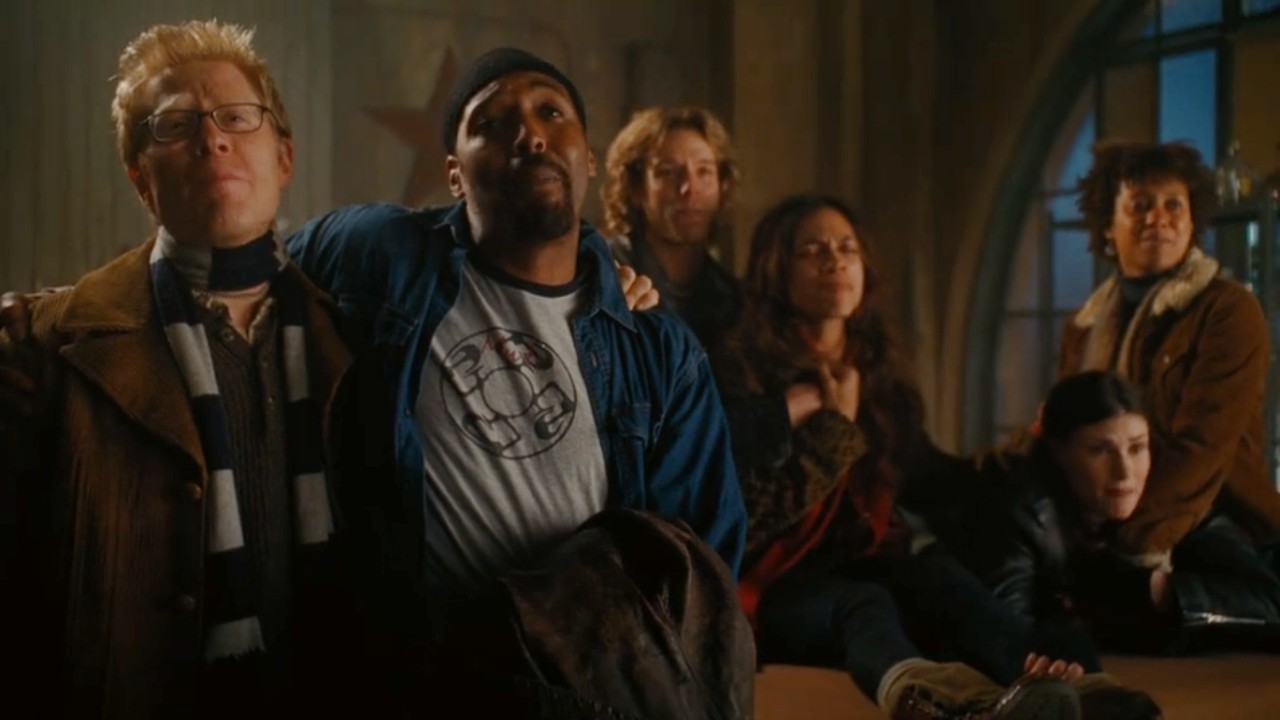 From left to right: Mark and Tom wholding each other's shoulders, Roger, Mimi, Maureen and Joanne are behind them.