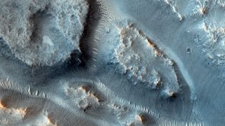 A close up of the surface of Mars showing blue dunes with streaks of ancient river basins between the dunes
