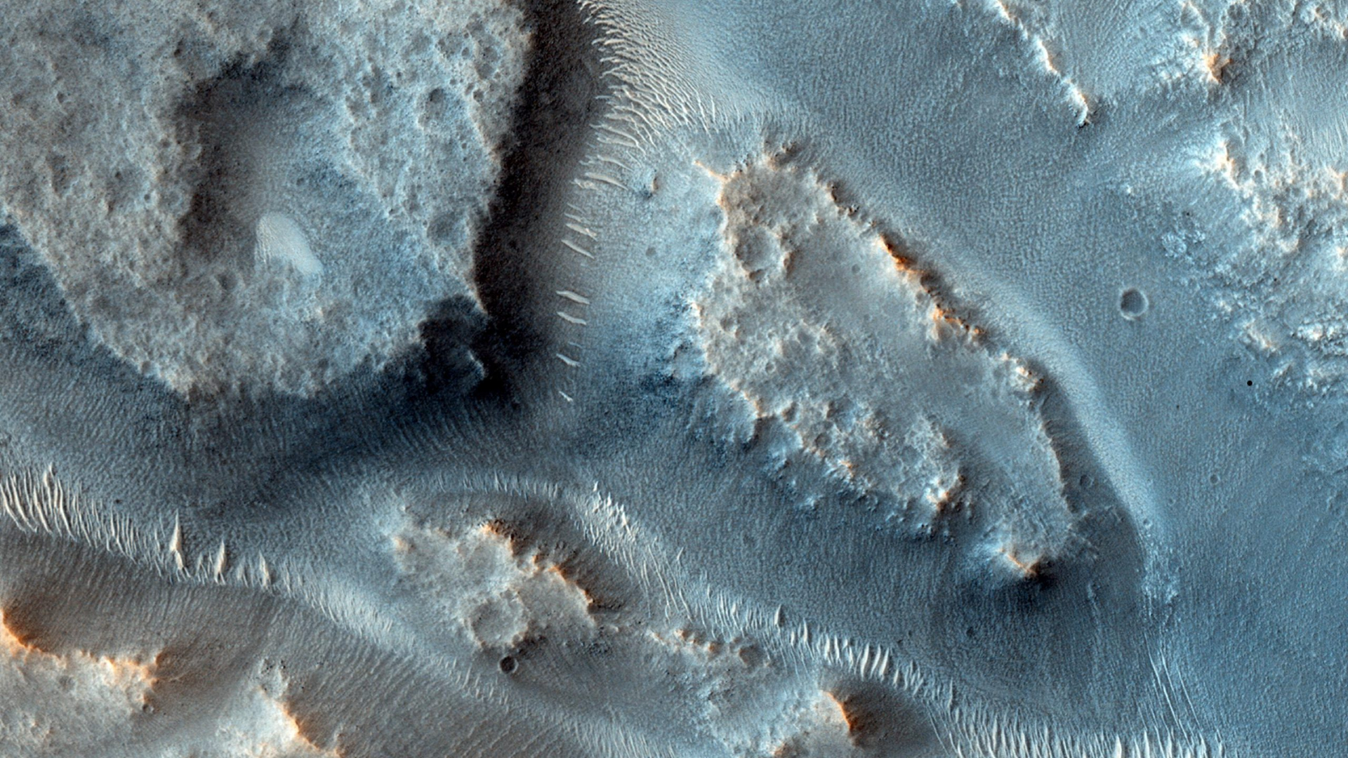 A close up of the surface of Mars showing blue dunes with streaks of ancient river basins between the dunes