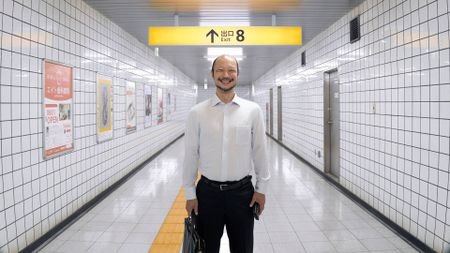 An image from Exit 8 showing a clean, bright passageway of a Japanese underground metro with a single suited man standing and smiling