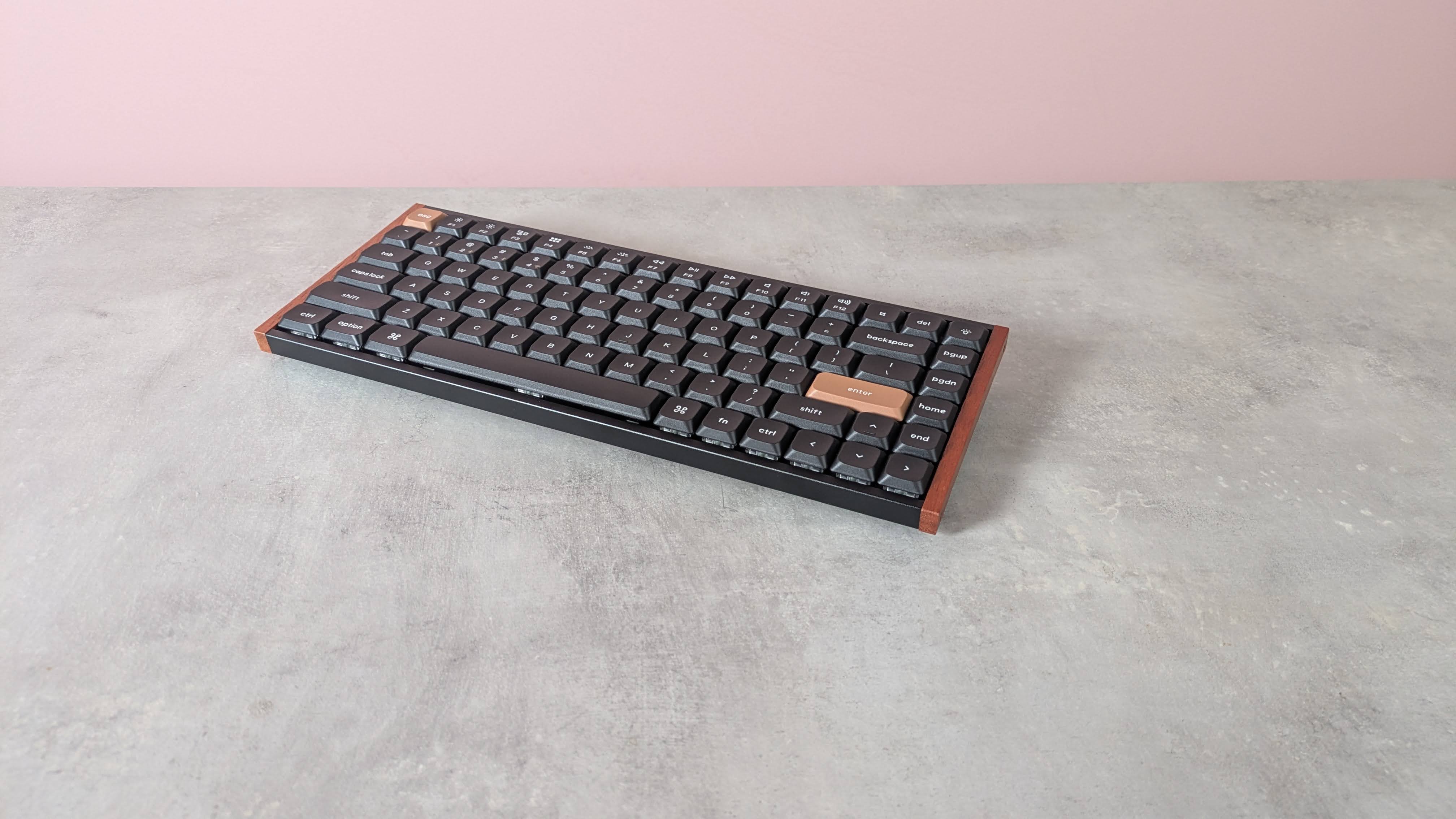 Three-quarter view of Keychron K3 HE on a desk with pink wall in background