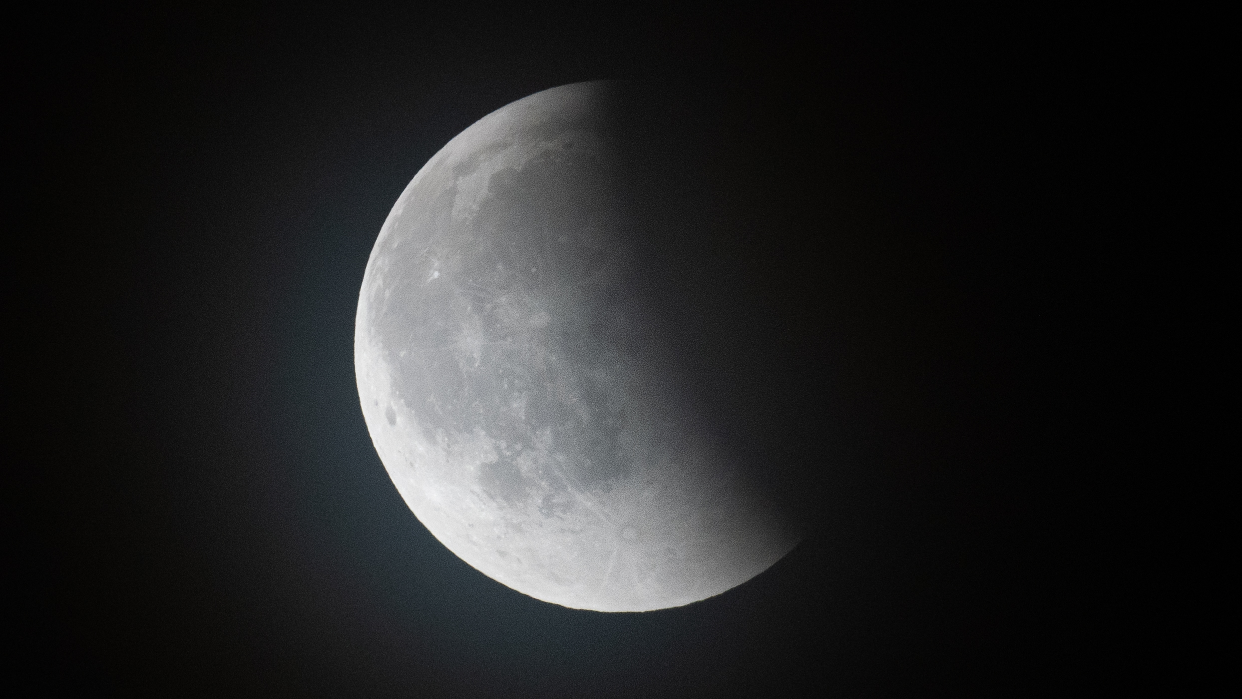 A full moon is shown against a dark sky with Earth's crescent shadow covering its eastern surface.