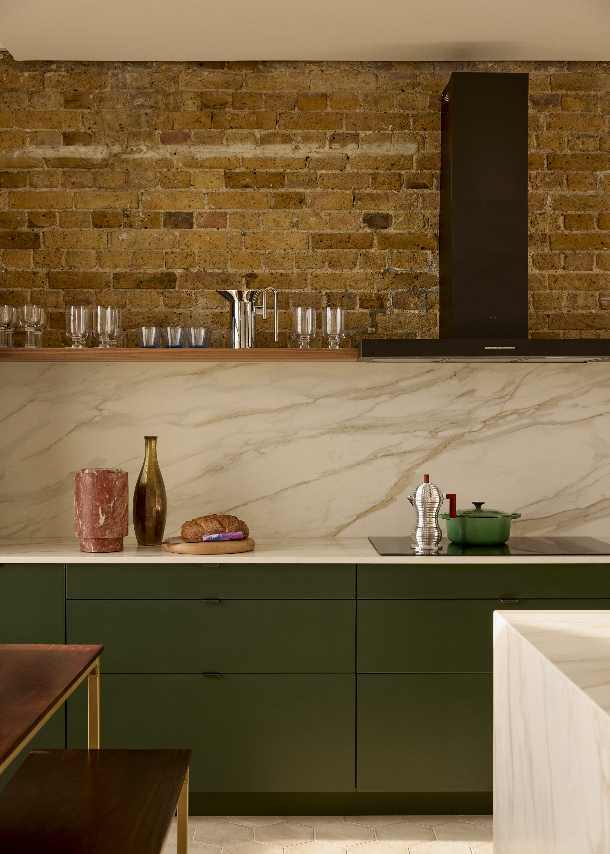 A small kitchen with green slab cabinetry, a marble countersplash, and an exposed brick wall
