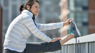 Woman stretches her leg on street barrier