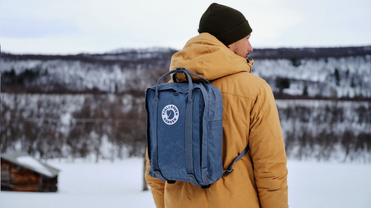 A man wearing a Fjallraven backpack looks at a snowy mountain