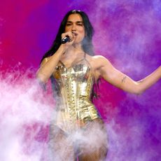 a woman with dark hair performing on stage at a concert in a metallic gold leotard