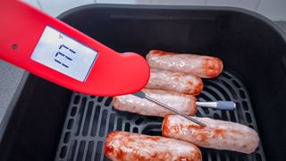 ThermoWorks Thermopen ONE thermometer being used to test the temperature of cooking sausages