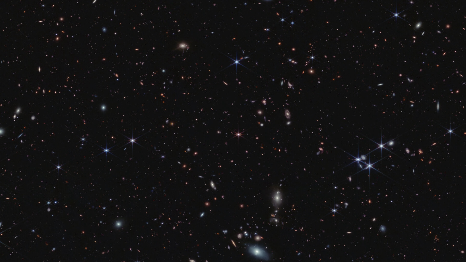 a deep field image with many galaxies with a pink spiky red dot in the center of the image