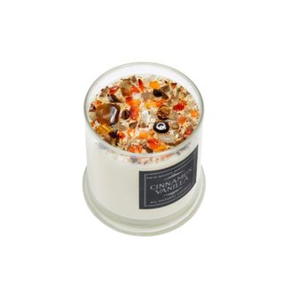 A white fall candle with orange decorations on top and a black label