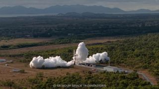 An aerial photo of a rocket taking off from a landing pad surrounded by smoke