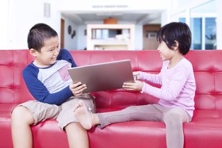 Young brother and sister fighting over a laptop.