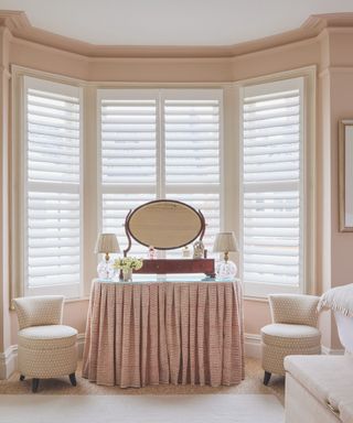 dressing area in bedroom in front of bay window with skirted cabinet