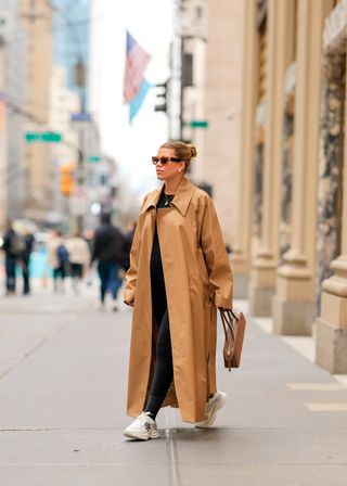 Sofia Richie Grainge wearing trench coat, black leggings, black t-shirt, and running shoes.