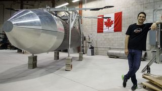 rocket prototype in silver on the left, canadian flag on the wall in behind, and a person leaning on equipment on the right