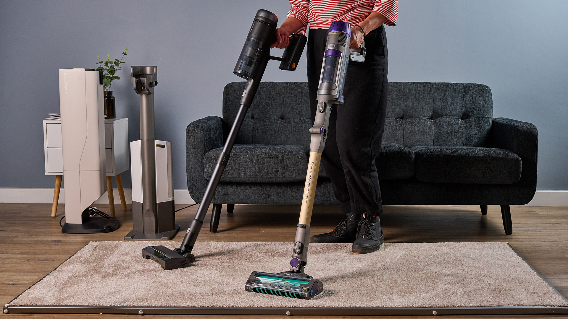 Homes Editor holding two vacuums with auto empty docks in the background