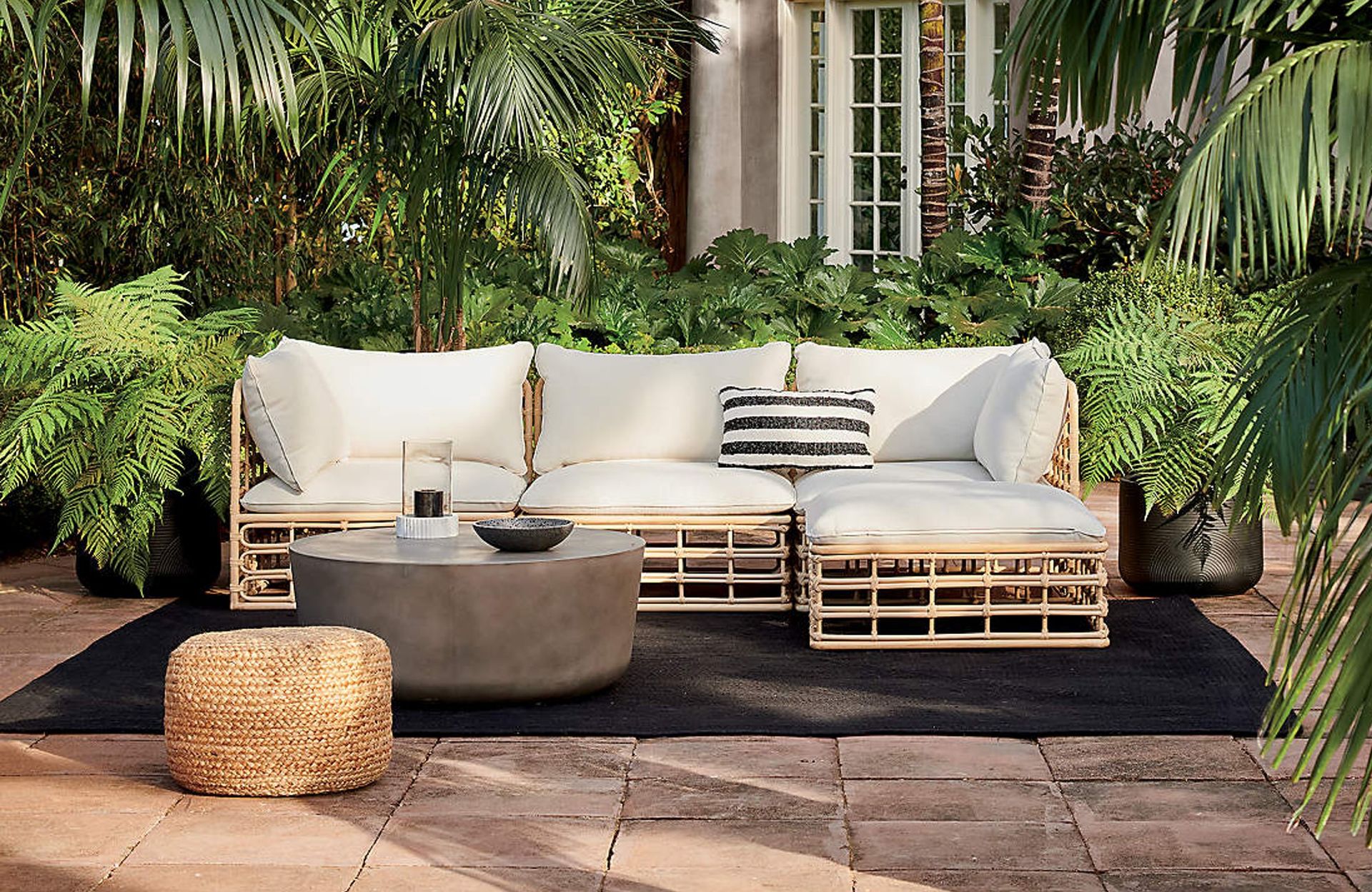 A wicker-effect outdoor sofa in a lush tropical backyard