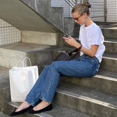 Woman looking at a phone wearing a white tee and jeans