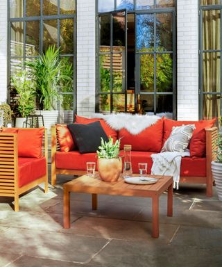 An outdoor sofa with red/orange outdoor cushions and wooden rectangular coffee table