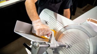 young man wearing plastic gloves and operating a meat slicer at a deli