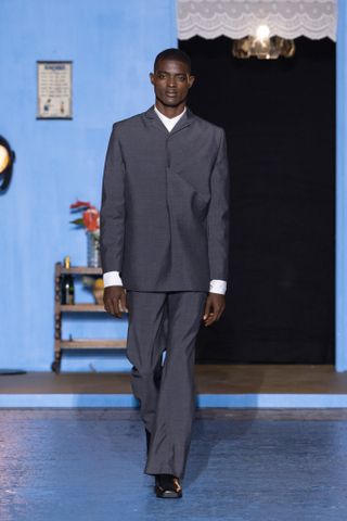 Man on Bianca Saunders runway in folded grey suit