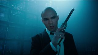 Still from the movie Superman (2025). Close up of Lex Luthor holding a gun as he moves forward cautiously. He is a bald man and is wearing a black and white tuxedo. In the dark background there are blue colouring lights that look like a computer server room