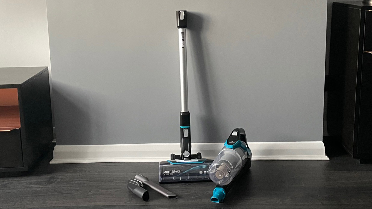 Bissell CleanView Pet Slim Cordless Stick Vacuum and all its accessories against a grey wall in a room with a grey floor