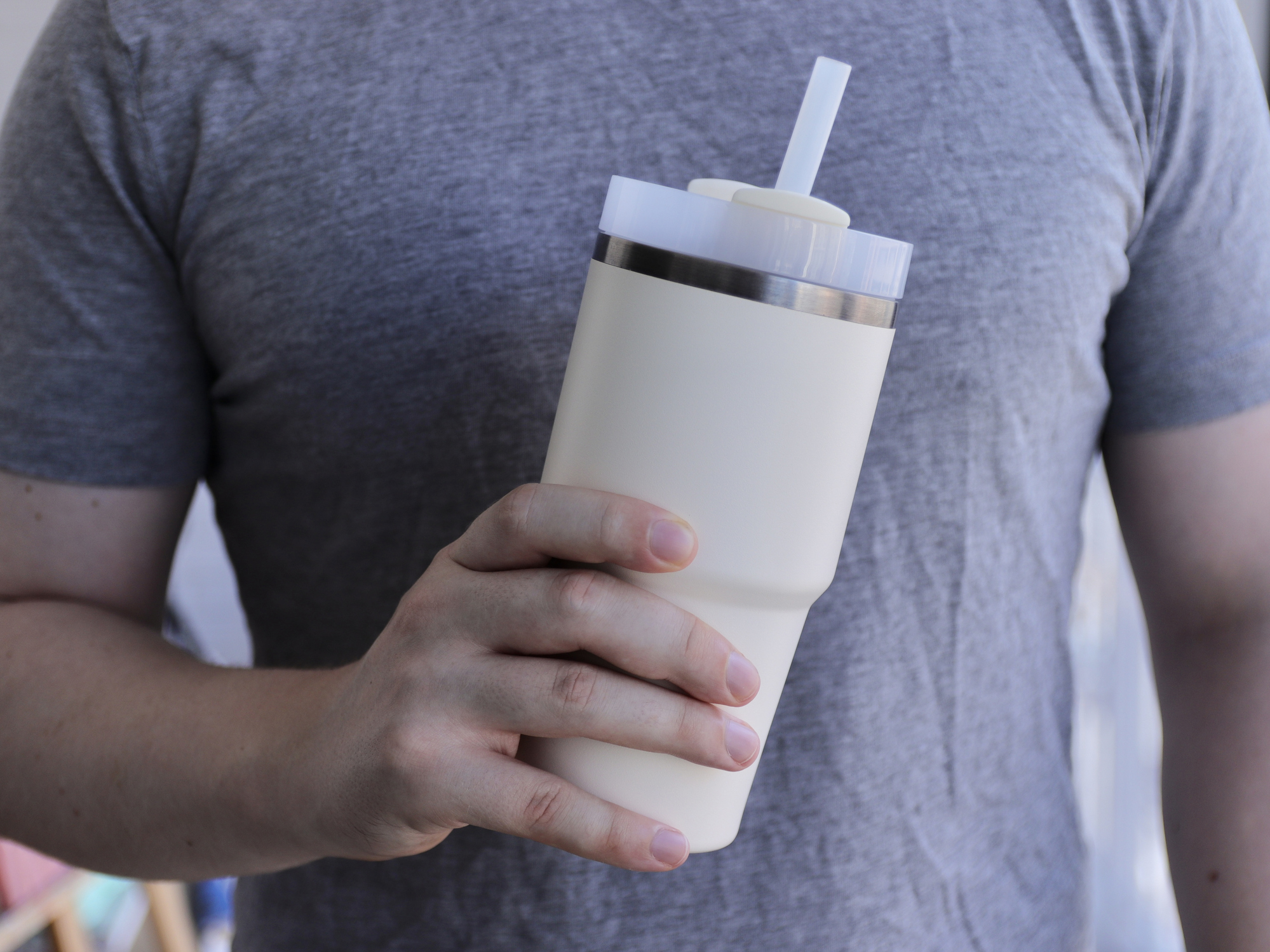 A man holding a cream Stanley Cup dupe with a straw.