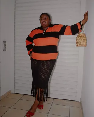 Influencer wears black and orange rugby shirt, sheer knit skirt, and red sandals.