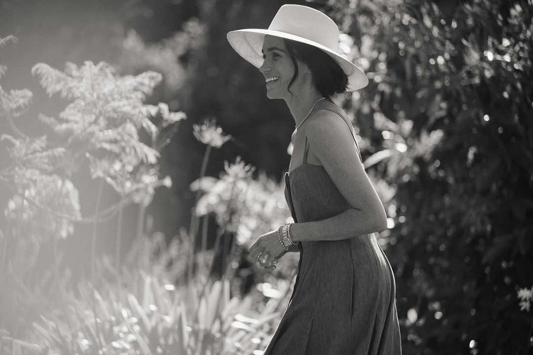 Meghan Markle wearing a sun hat and dress in a garden and smiling