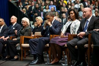 President Barack Obama, First Lady Michelle Obama and Mark Kelly (at far right), the husband of Rep. Gabrielle Giffords, listen to remarks by Daniel Hernandez, the intern who helped save the life of Rep. Giffords during the Tucson shootings. This memorial