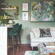 A sage green-painted living room with a botanical-print sofa and a green artwork hanging on the wall