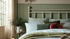 A bedroom with sage green panelling, a cream iron bed frame, and blue and green bedding