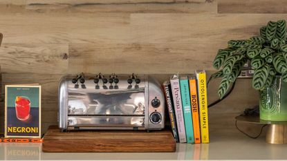 bright cookbooks lenaing against a stainless steel toaster on a kitchen counter